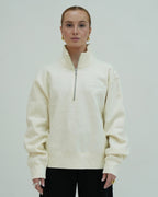 Person wearing a cream-colored half-zip sweatshirt against a plain background