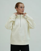 Woman wearing a cream-colored hoodie with a zipper on a plain background