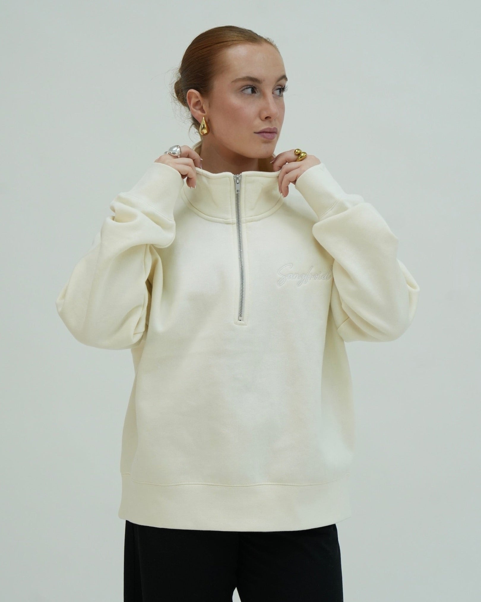 Woman wearing a cream-colored hoodie with a zipper on a plain background