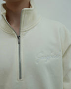 Close-up of a cream-colored fleece pullover with a zipper and 'Sangfroid' branding.