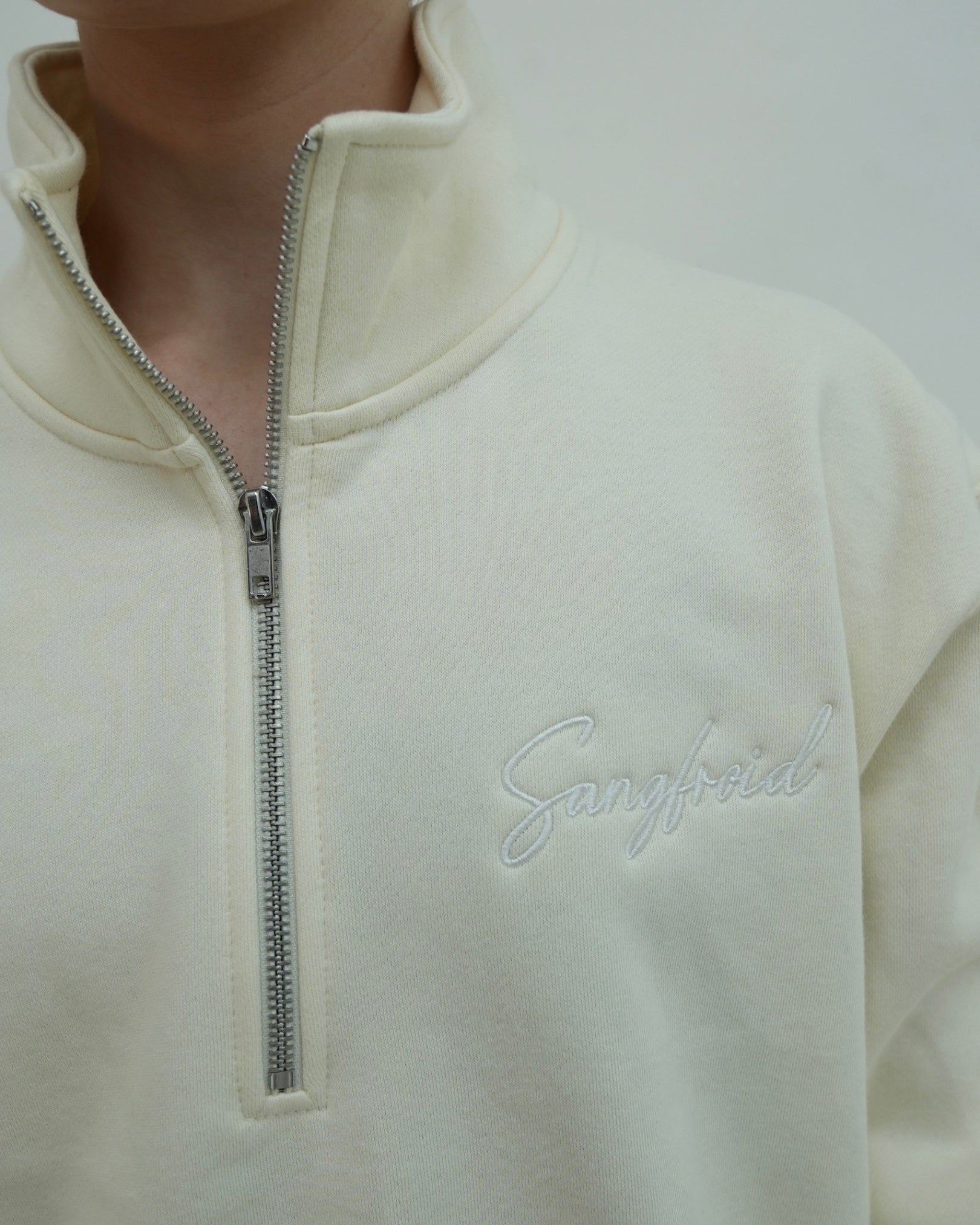 Close-up of a cream-colored fleece pullover with a zipper and 'Sangfroid' branding.