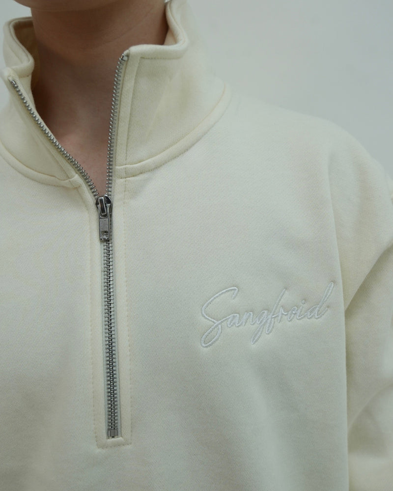 Close-up of a cream-colored fleece pullover with a zipper and 'Sangfroid' branding.
