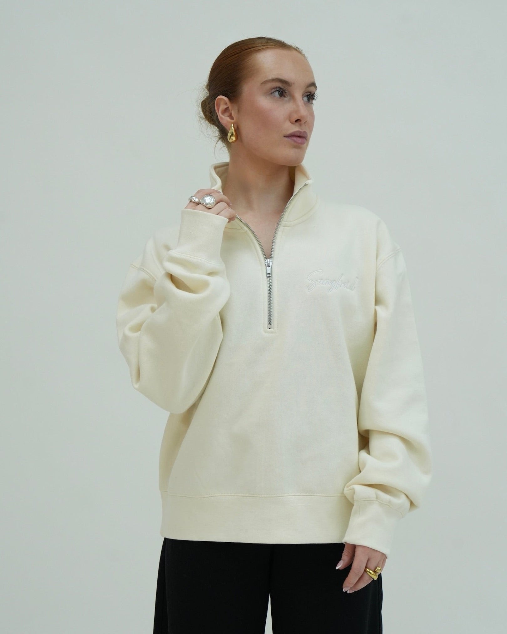 Woman wearing a cream-colored pullover with a zipper against a plain background
