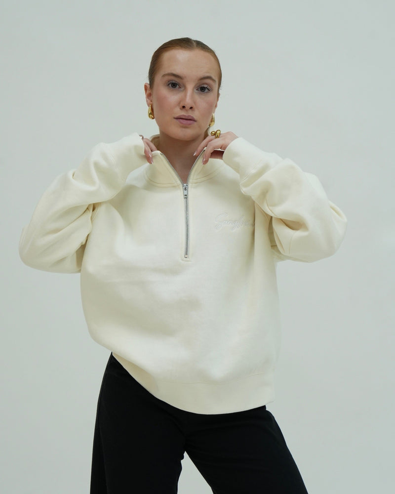 Person wearing a cream-colored sweater with a zipper on a plain background