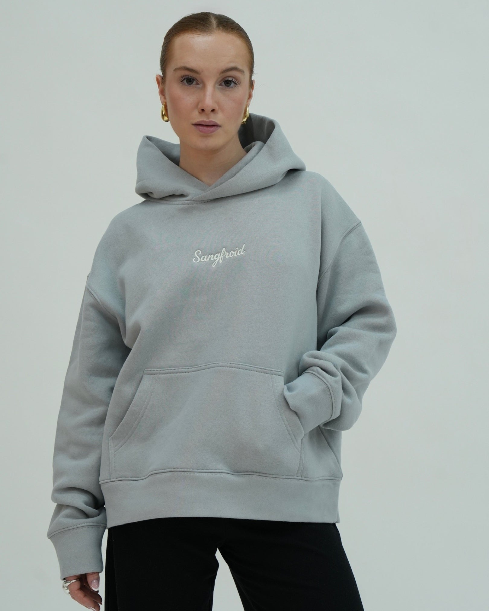 Person wearing a gray hoodie with 'Sangfroid' text on a plain background