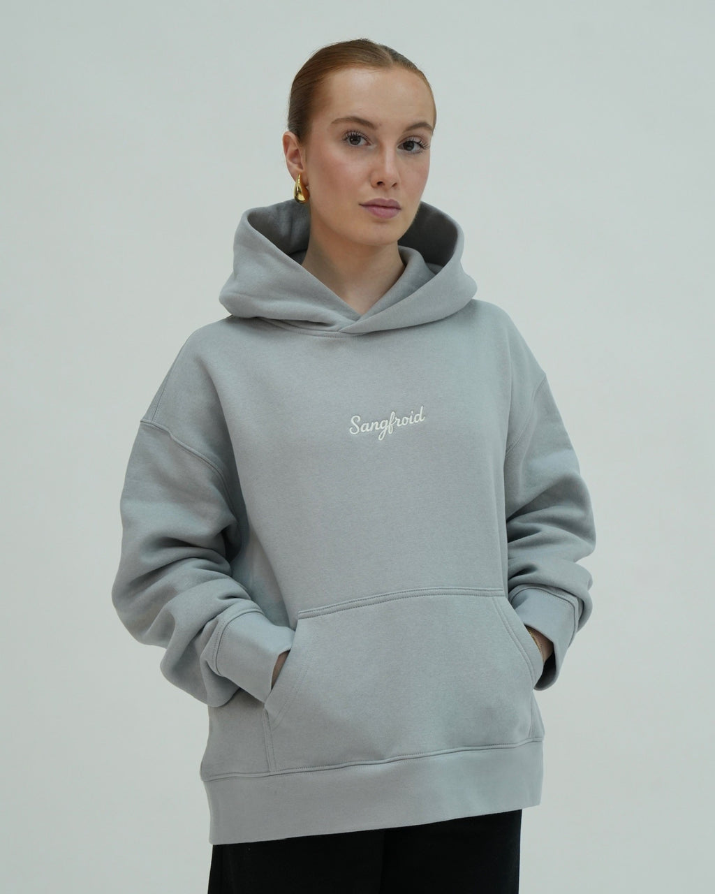 Person wearing a light gray hoodie with 'Sangfroid' text on a plain background