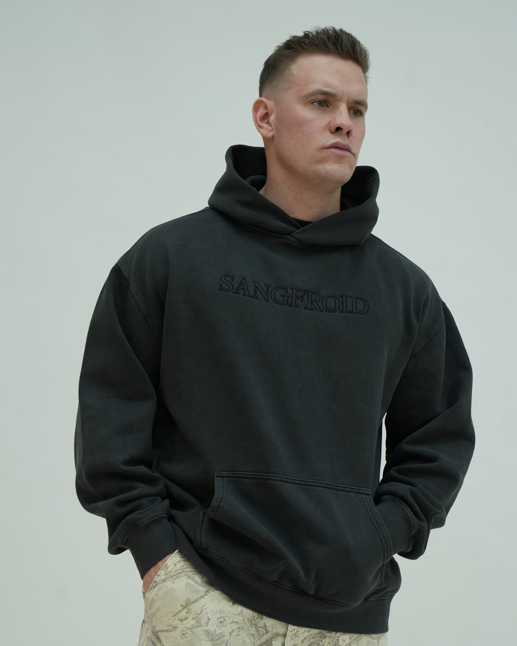 Man wearing a black hoodie with 'SANGFROID' text on a plain background