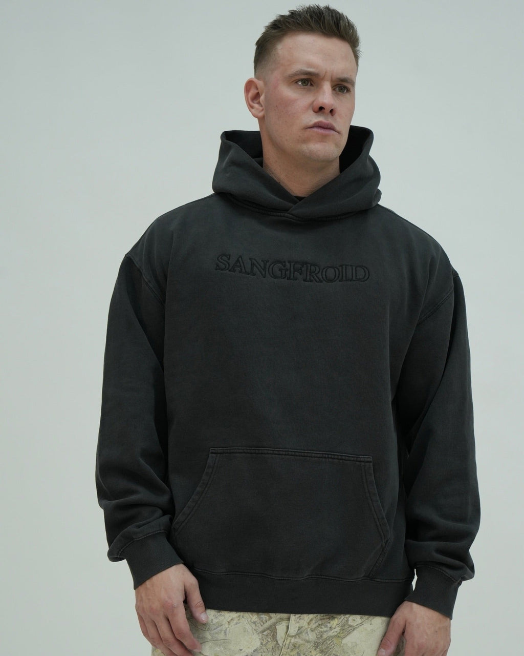 Man wearing a black hoodie with 'SANGFROID' branding on a plain background