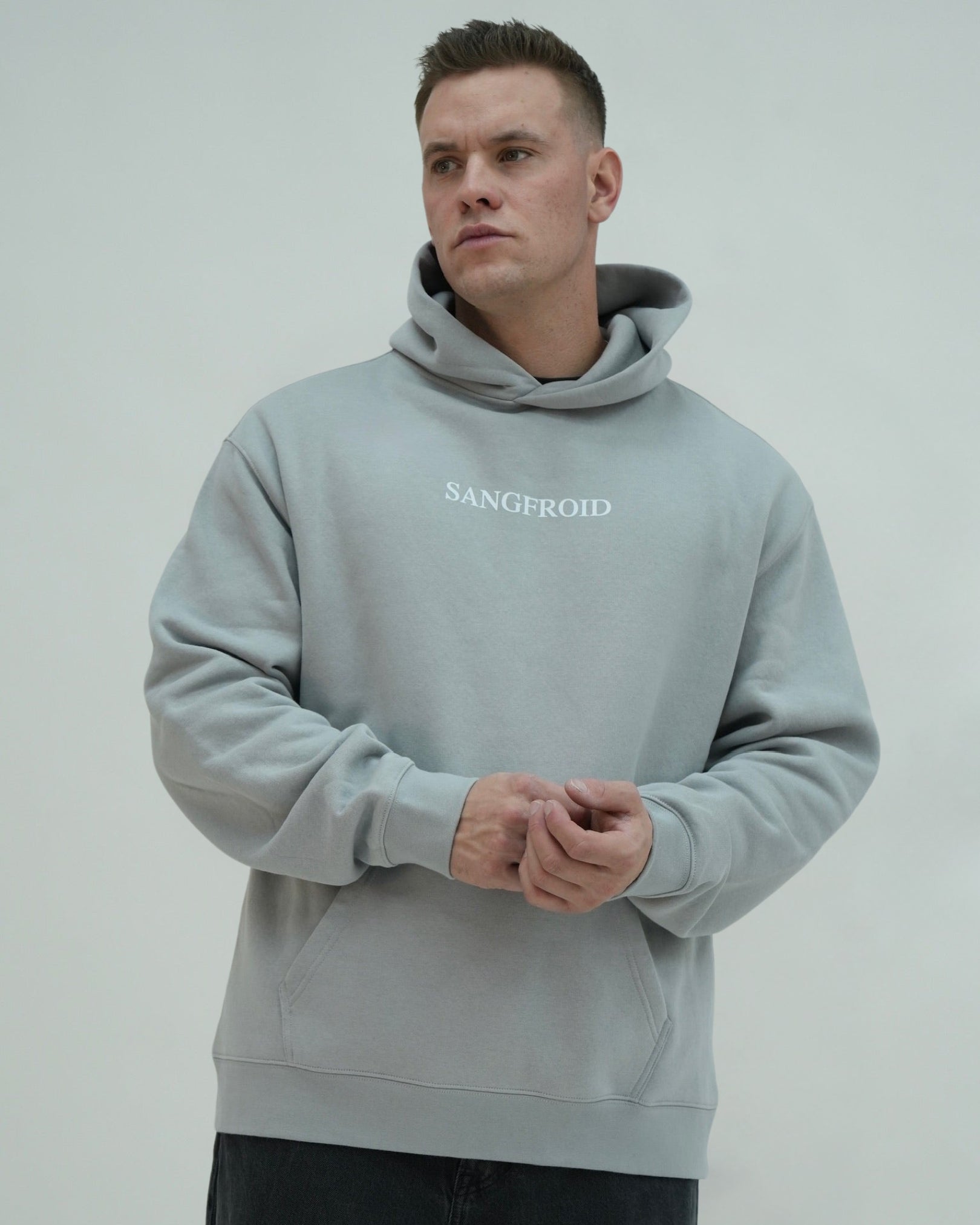 Man wearing a light gray hoodie with 'SANGFROID' text on a plain background