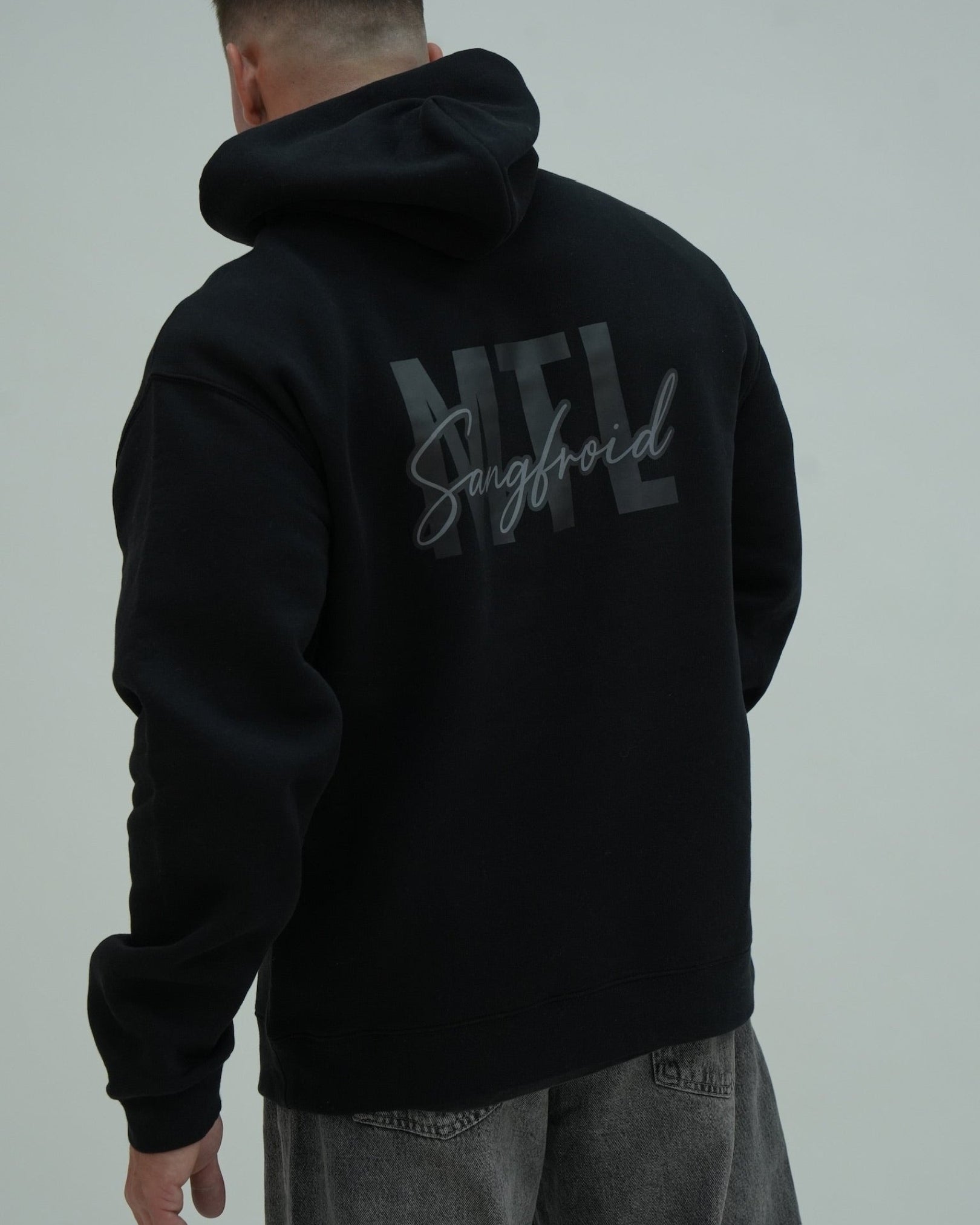 Person wearing a black hoodie with 'MTL Sangfroid' text on the back against a gray background
