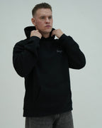 Man wearing a black hoodie with a brand logo on a light gray background