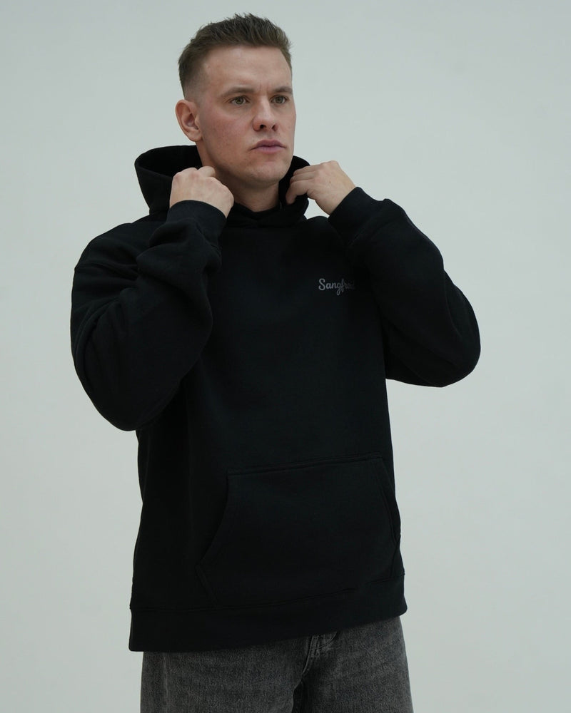 Man wearing a black hoodie with a brand logo on a light gray background