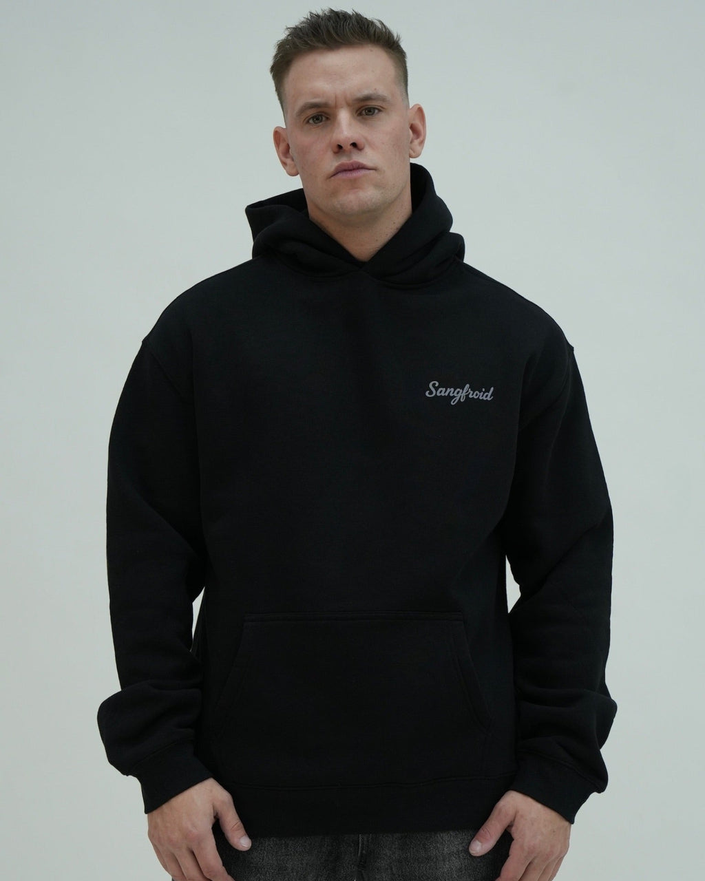 Man wearing a black hoodie with 'Sangfroid' branding on a plain background