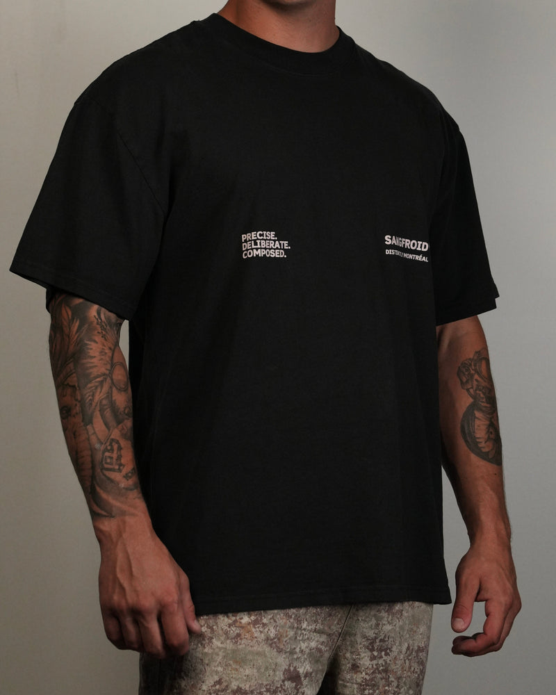 Person wearing a black t-shirt with text and logos on a plain background