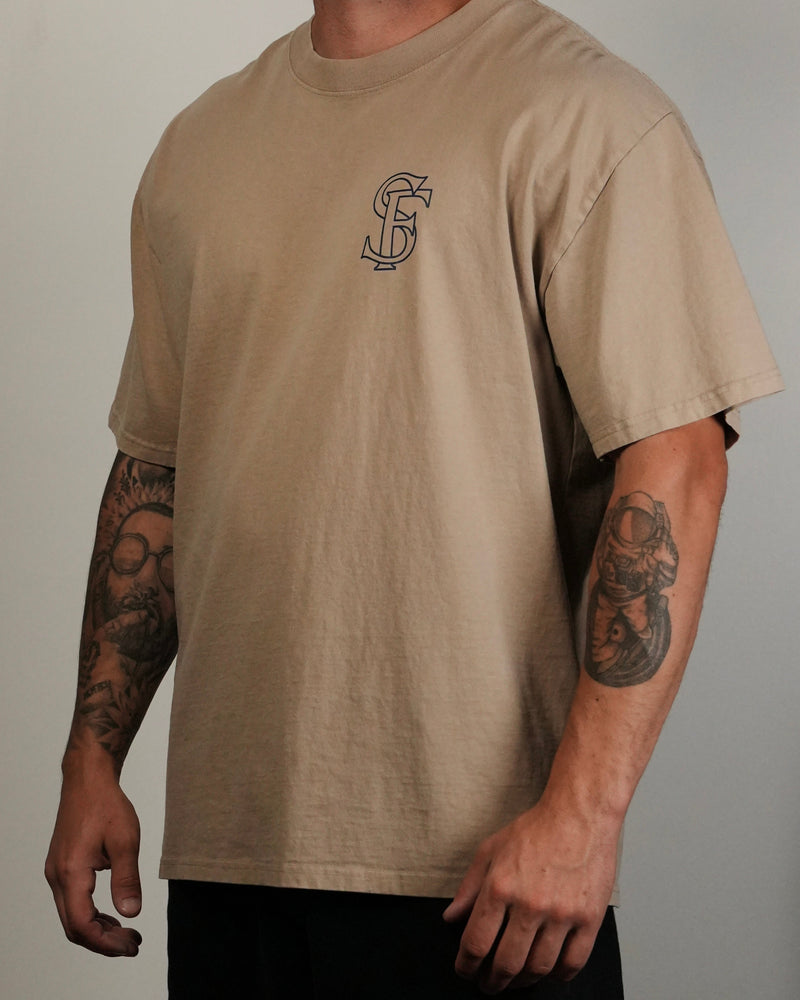Person wearing a beige t-shirt with a logo on a plain background